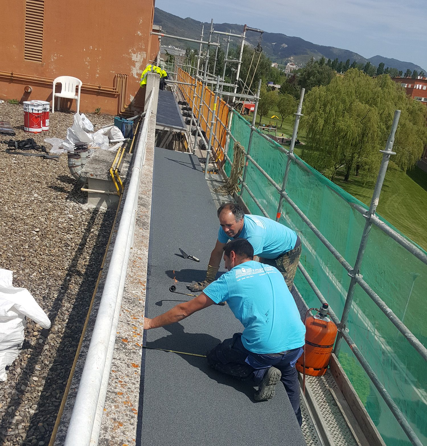 Proyecto de Rehabilitación de fachada y aleros de un bloque de viviendas del barrio de Mendillorri de Pamplona (Navarra). Operarios trabajando en la instalación de tela asfáltica de uno de los aleros del edificio.