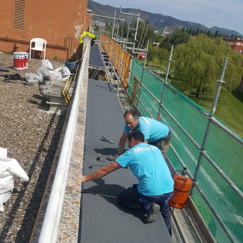 Proyecto de Rehabilitación de fachada y aleros de un bloque de viviendas del barrio de Mendillorri de Pamplona (Navarra). Operarios trabajando en la instalación de tela asfáltica de uno de los aleros del edificio.