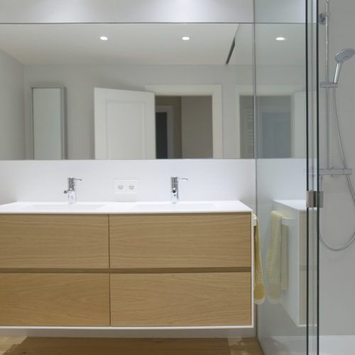 Proyecto de Reforma íntegra de baño en una vivienda de Pamplona (Navarra). Paredes y techo en blanco y suelo en madera de haya. Lavabo doble y mampara de vidrio. Un espacio cálido y limpio.